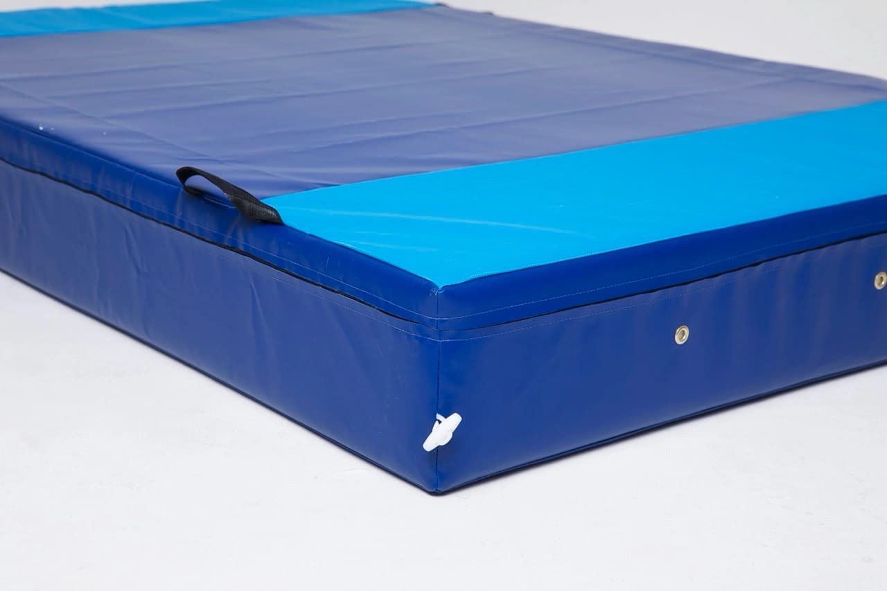 Blue mat with a light blue top edge, black carry handle, metal grommets along the side, and a white corner valve.
